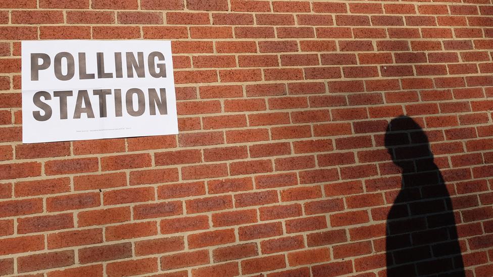 The shadow of a man going to vote is cast on a wall outside a polling centre in a bowling club on May 7, 2015 in Redcar