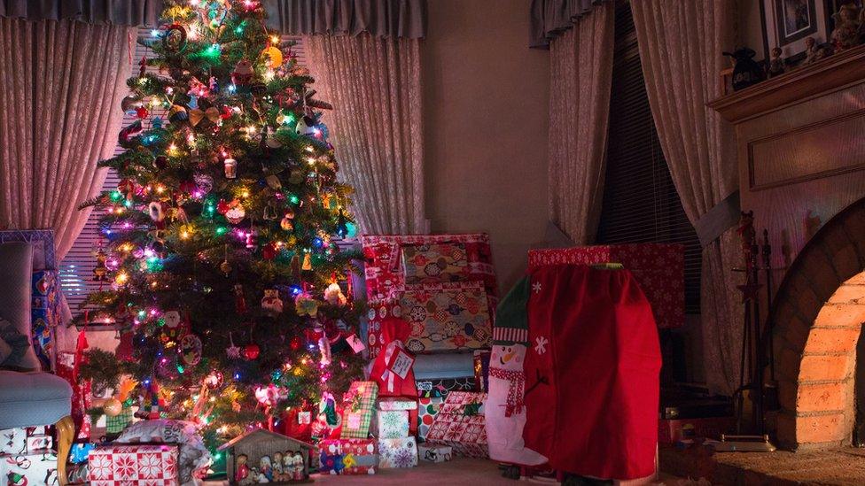 A Christmas tree with lights on surrounded by presents