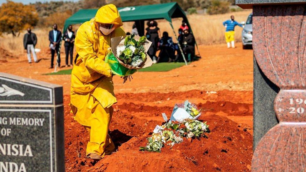 An undertaker wearing personal protective equipment (PPE) lays flowers on the grave containing the remains of Modise Motlhabane, who died of COVID-19 coronavirus, during the funeral at the Westpark cemetery in Johannesburg, on July 22, 2020.