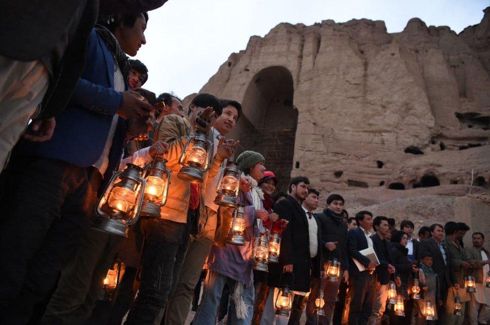 People holding lanterns stand beside the cliff