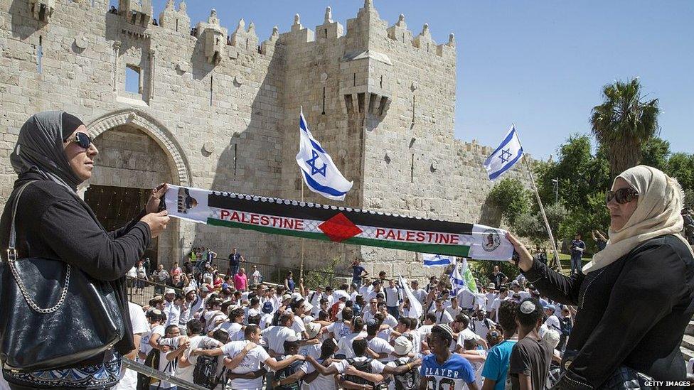 Palestinian women hold a scarf bearing the Palestine name as Israeli youths hold their national flag near Damascus Gate in Jerusalem's old city during Jerusalem Day