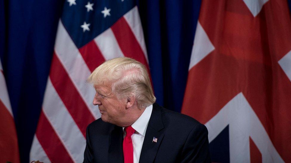 US President Donald Trump sitting in front of an American and UK flag