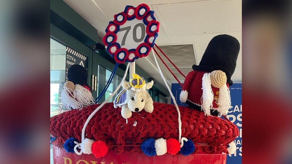 A knitted post box topper showing Beefeaters, a corgi and a maypole in Crowborough