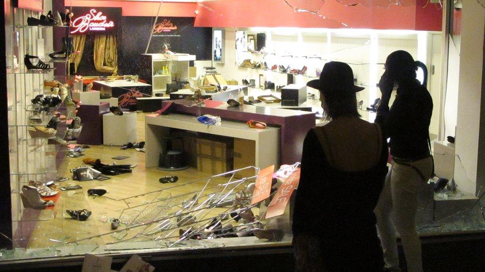 Two people look at a looted shoe shop