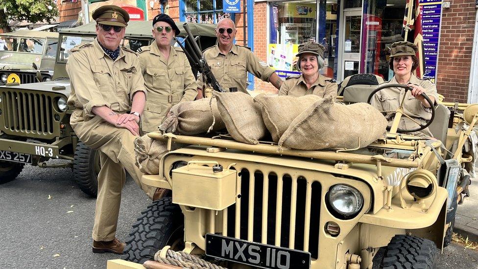 Men and women dressed in 1940s military uniform with two women driving a military jeep