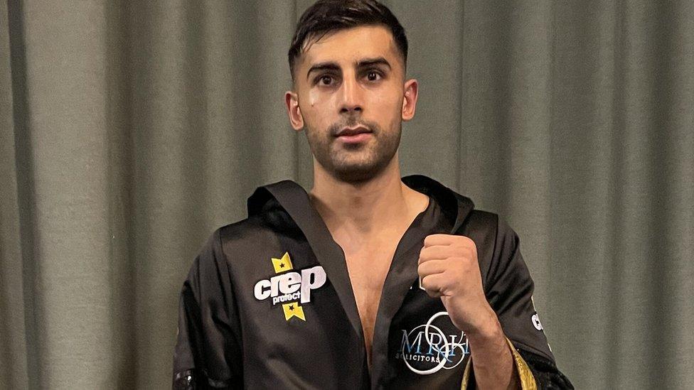 Khaleel Majid looks at the camera, he is wearing a boxing robe and one of his fists is clenched