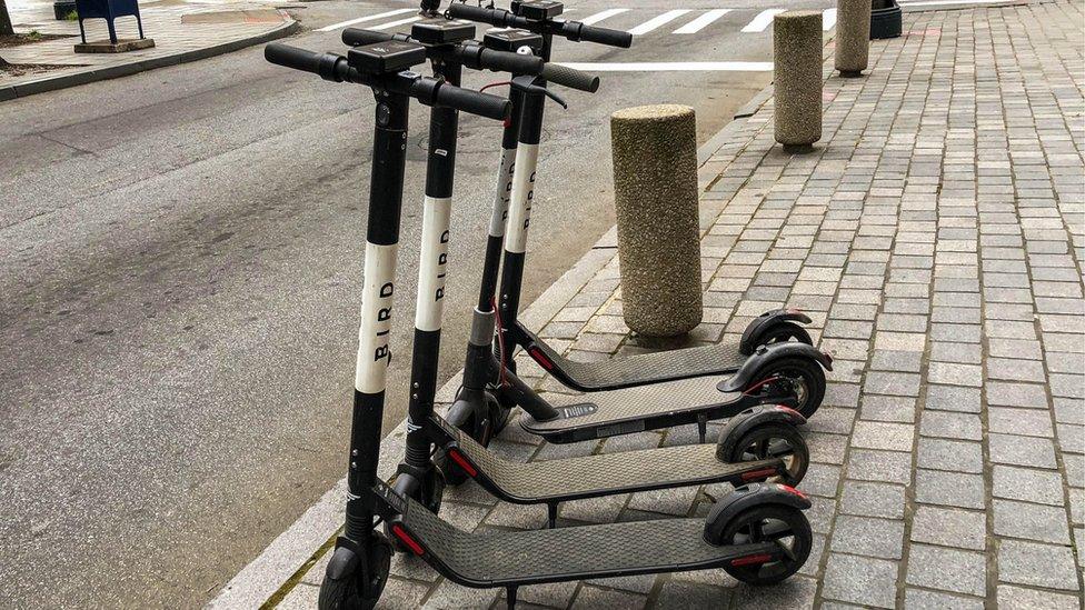 Four electric scooters are shown lined up on the side of the street.