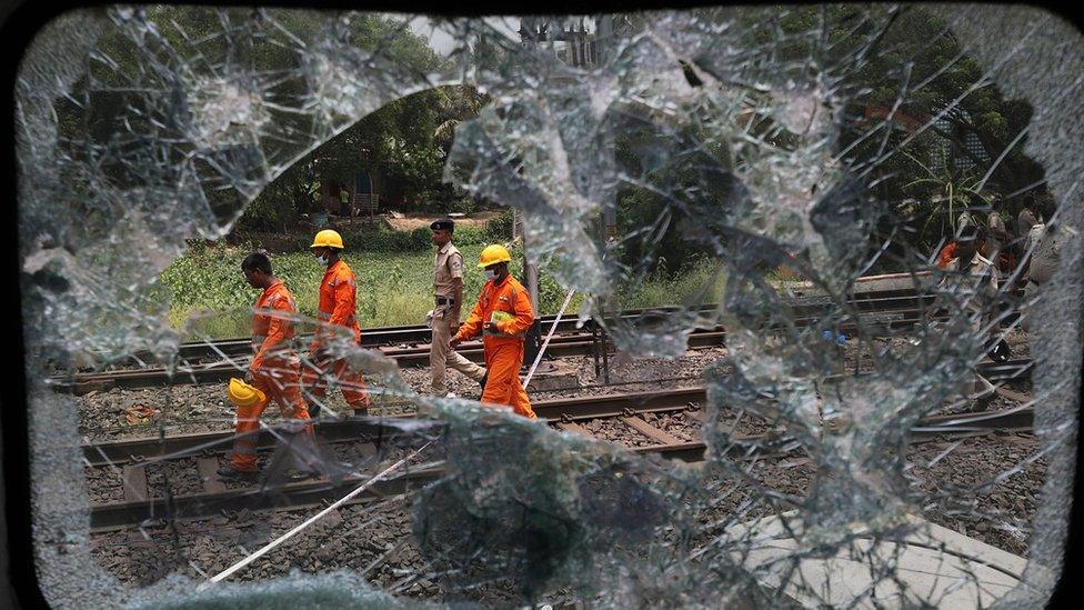 Rescue workers walk along the tracks, seen through a shattered window from the carriage