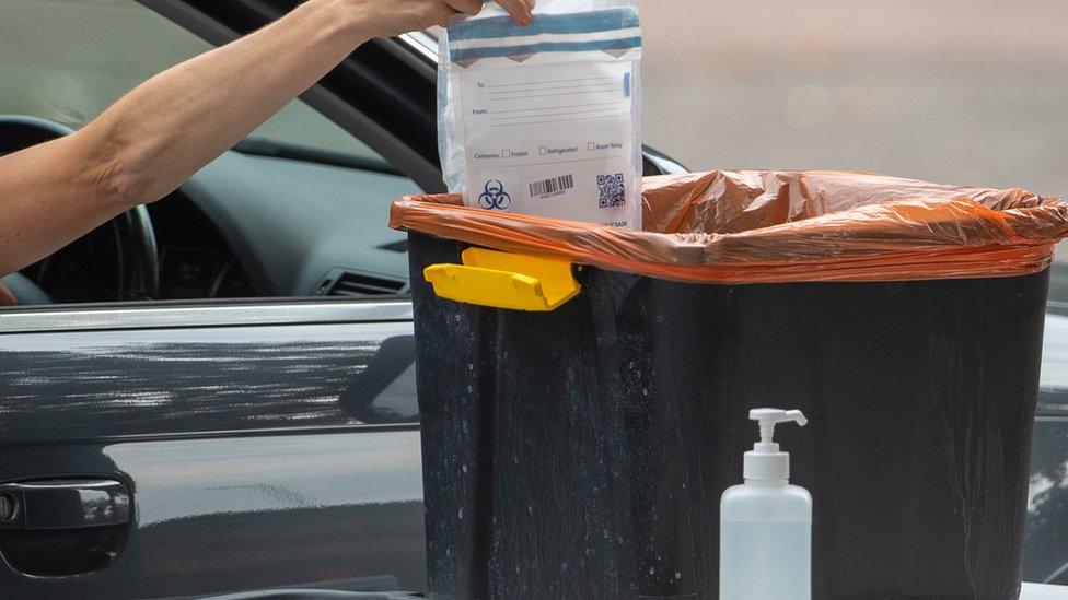 A person places a completed coronavirus test into a collection bin