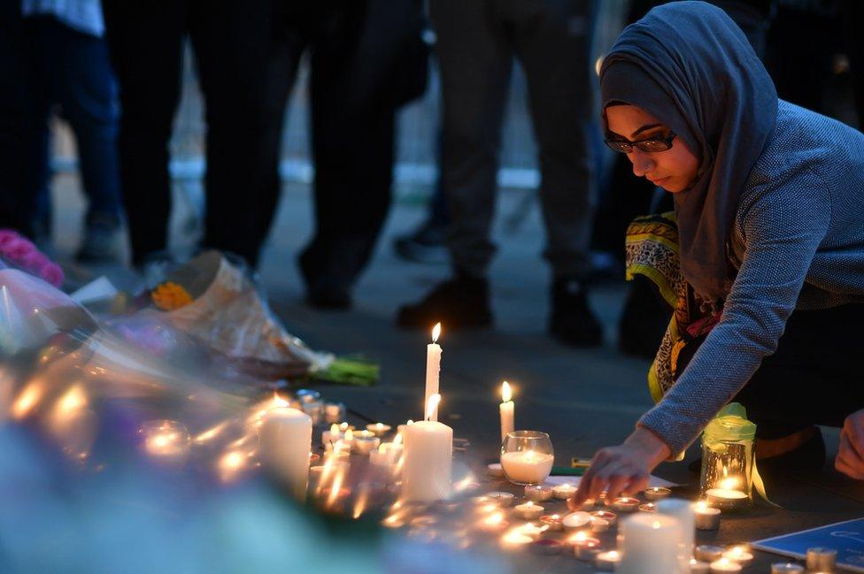 A woman lights candles set up in front of floral tributes in Albert Square in Manchester