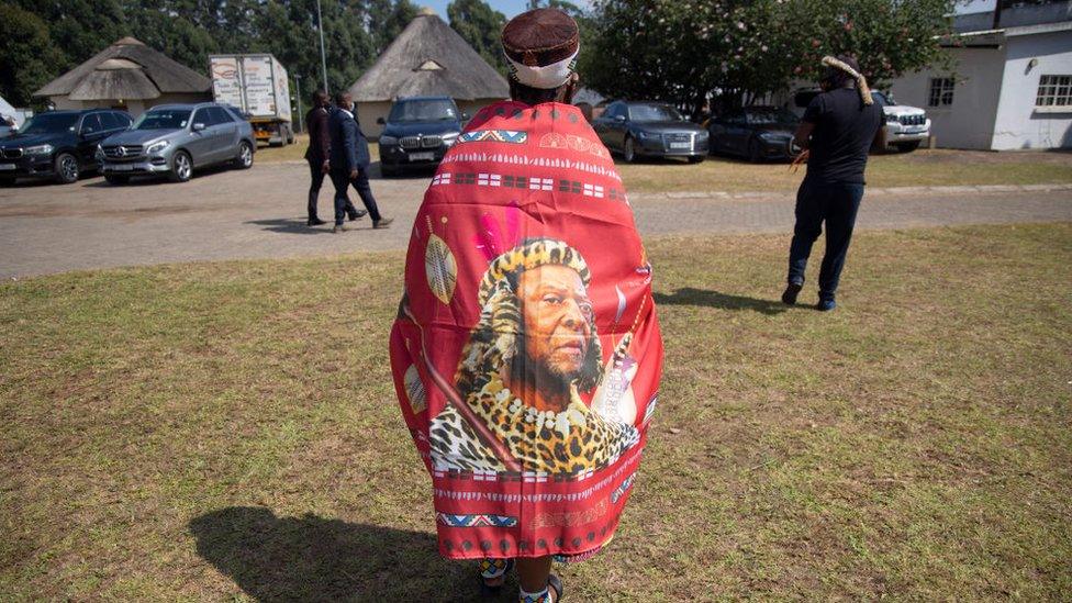 An elderly Zulu woman wearing a cloth reflecting the face of King Goodwill Zwelithini walks inside the KwaKhethomthandayo royal palace during his memorial service in Nongoma, South Africa, on March 18, 2021. - King Goodwill Zwelithini died on March 12, 2021 in the eastern city of Durban, aged 72, after weeks of treatment for a diabetes-related illness.His remains have been taken back to his birthplace, the small southeastern town of Nongoma in Kwa-Zulu Natal province, where he will be laid to rest after midnight.