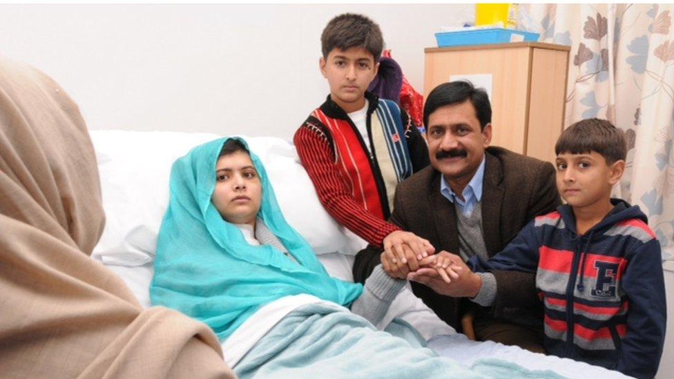 Malala lying in a Birmingham hospital bed surrounded by her family