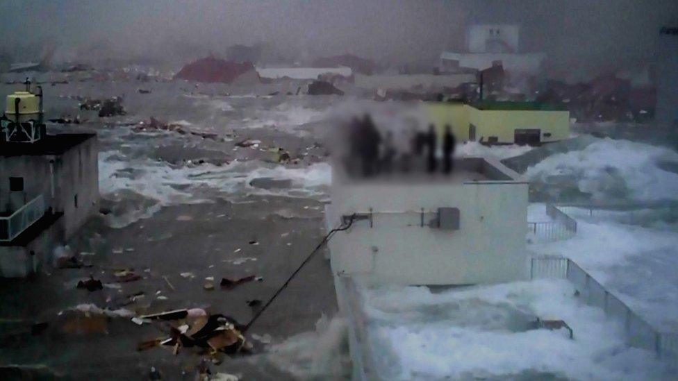 An image taken by local resident Yoshinori Hara shows the bank employees trapped on the roof by the rising water