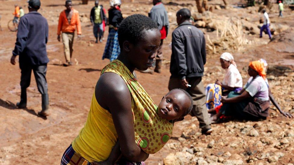 A woman carries her child as she walks near destroyed houses by flooding water after a dam burst, in Solio town near Nakuru, Kenya on 10 May 2018.