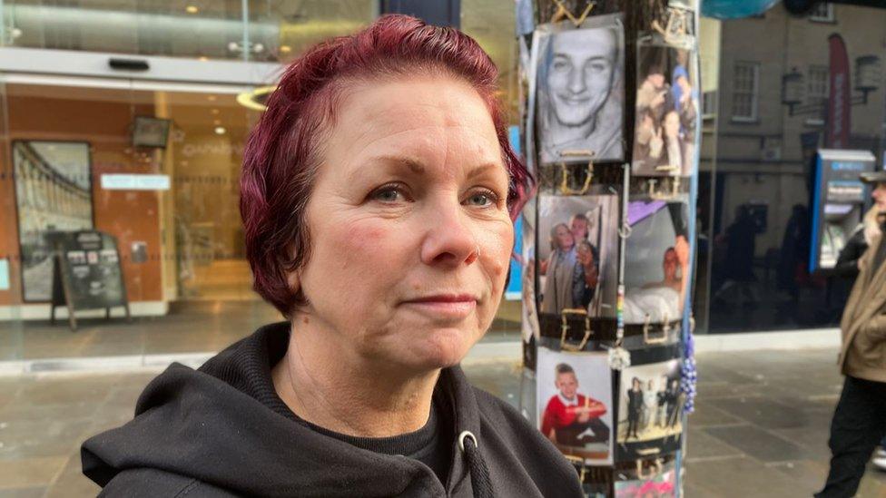 Mum stands in front of memorial on tree