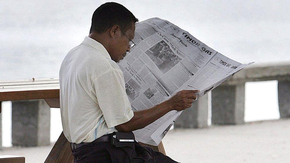 A man reads a newspaper at the beach in front of the government office in Dili