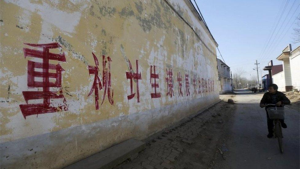 A resident rides a bicycle past a slogan on the wall which partially read "Pay attention to One-Child Policy and seek developments", at a village in Handan, Hebei province, China, December 2014.