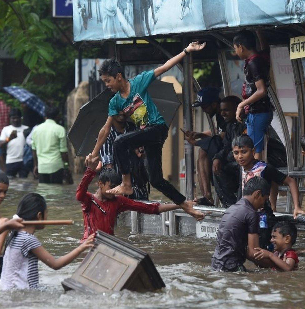 Indian children jump into the water of a flooded street after heavy rain showers in Mumbai on July 1, 2019