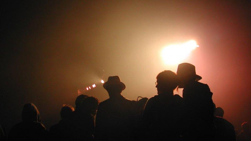 People silhouetted against stage lights waiting for a gig to begin