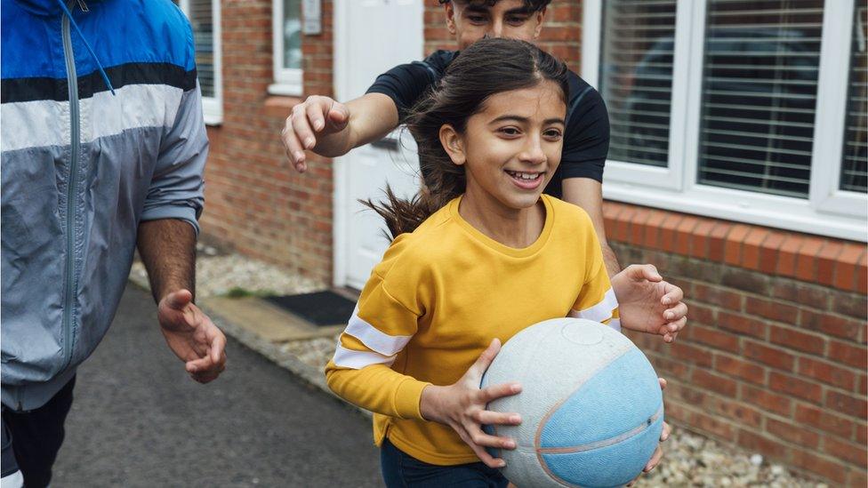 Girl plays basketball with dad and brother