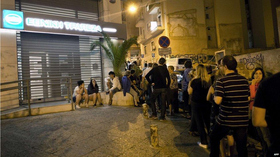 Greek people queue in front of an ATM in Athens