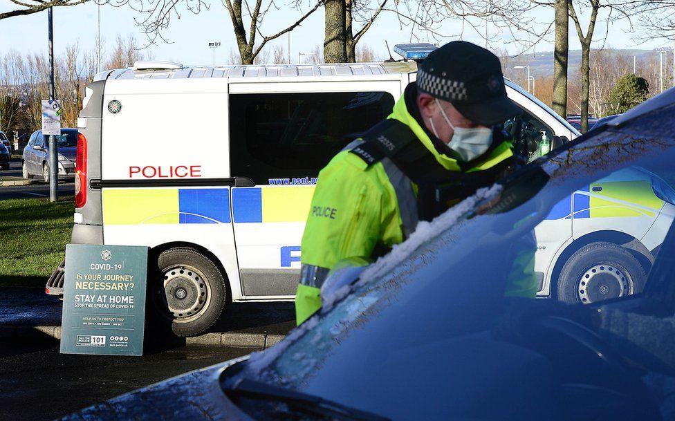 A masked police officer speaker to the driver of a car