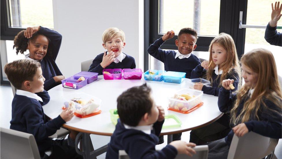 Elevated view of primary school kids sitting together at a round table eating their packed lunches