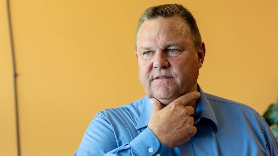 Jon Tester holds hand to face, wearing a blue shirt