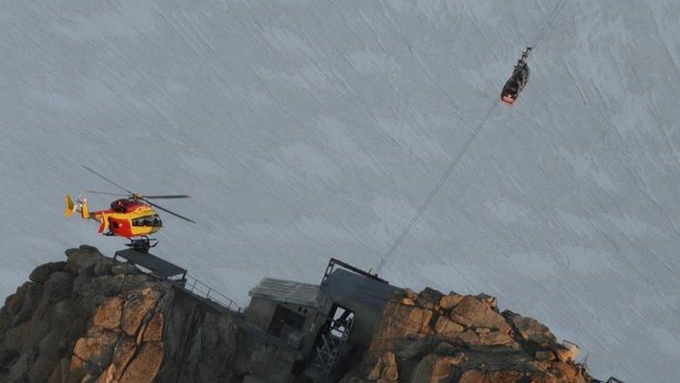 An EC-135 helicopter operated by French rescuers hovers near three cars suspended near Mont Blanc