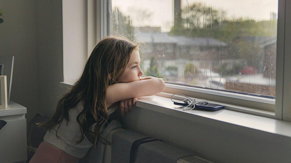 Young girl looking out of window at rain