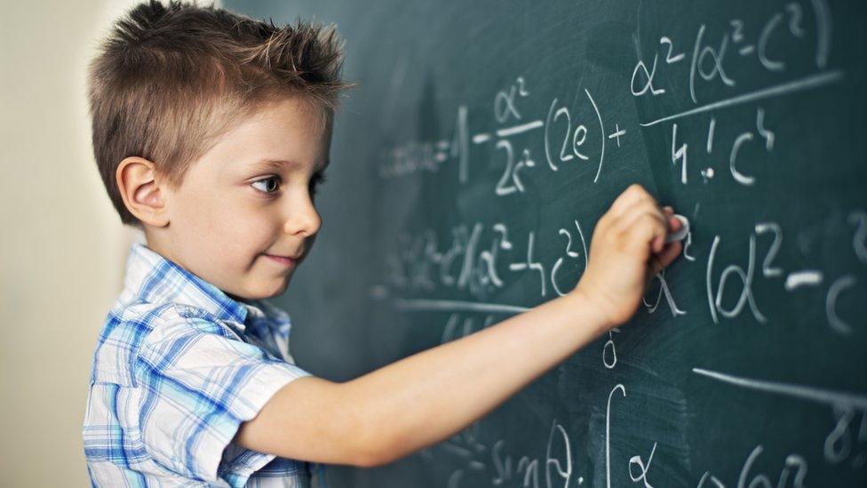 A young boy doing maths on a chalkboard