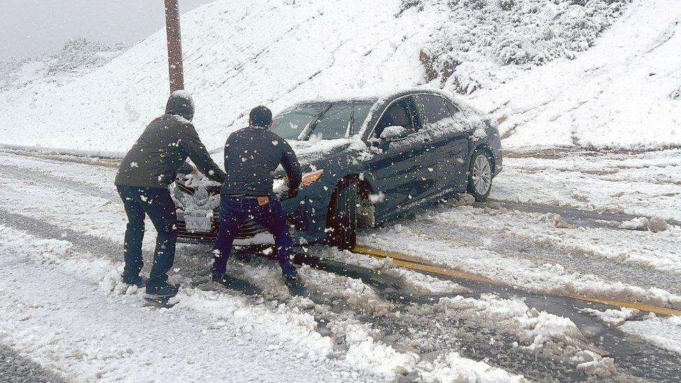 Two men try to stop a car from sliding down an icy roads during a snow storm in Rancho Cucamonga, California. Photo: 25 February 2023