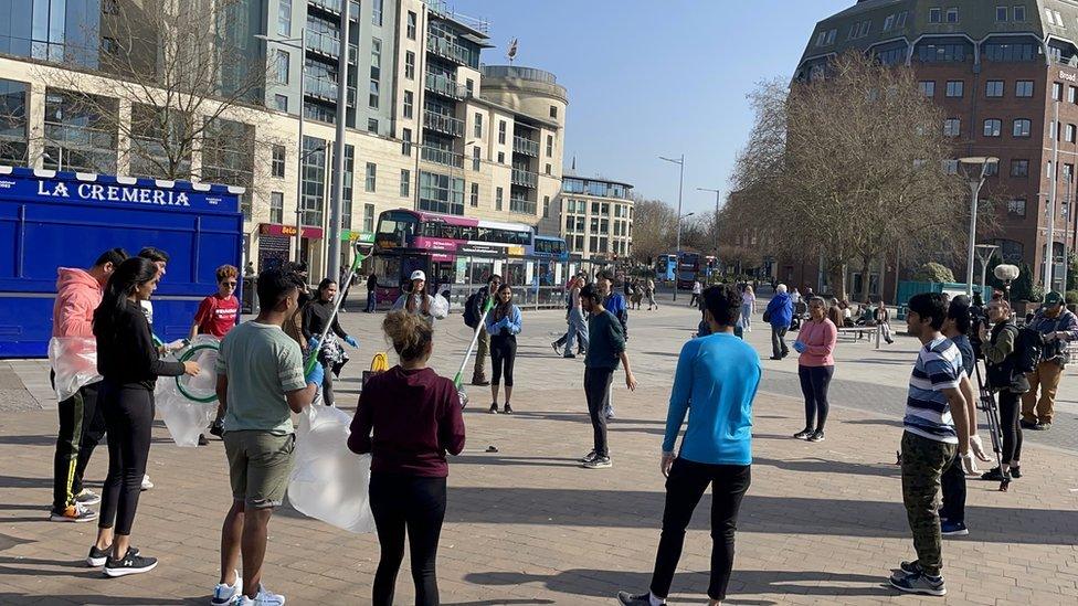 Lots of litter picking volunteers stand around Vivek Gurav listening to his session in the centre of Bristol