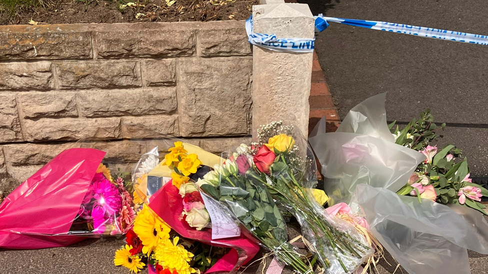 Floral tributes by police tape