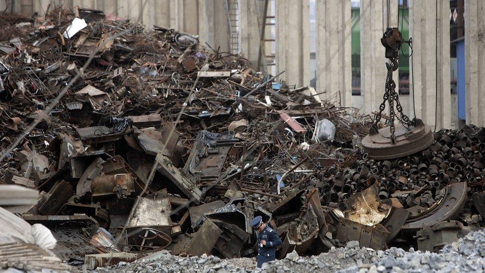 A security guard walks past a vast pile of scrap metal outside the Qinghe Special Steel Corporation plant