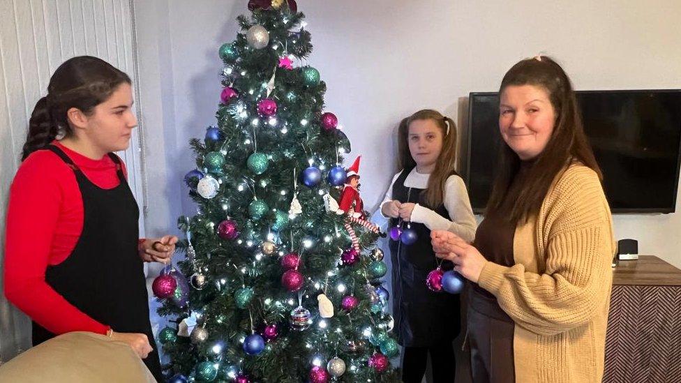 Girl with black hair and girl with brown hair decorating tree with woman with brown hair