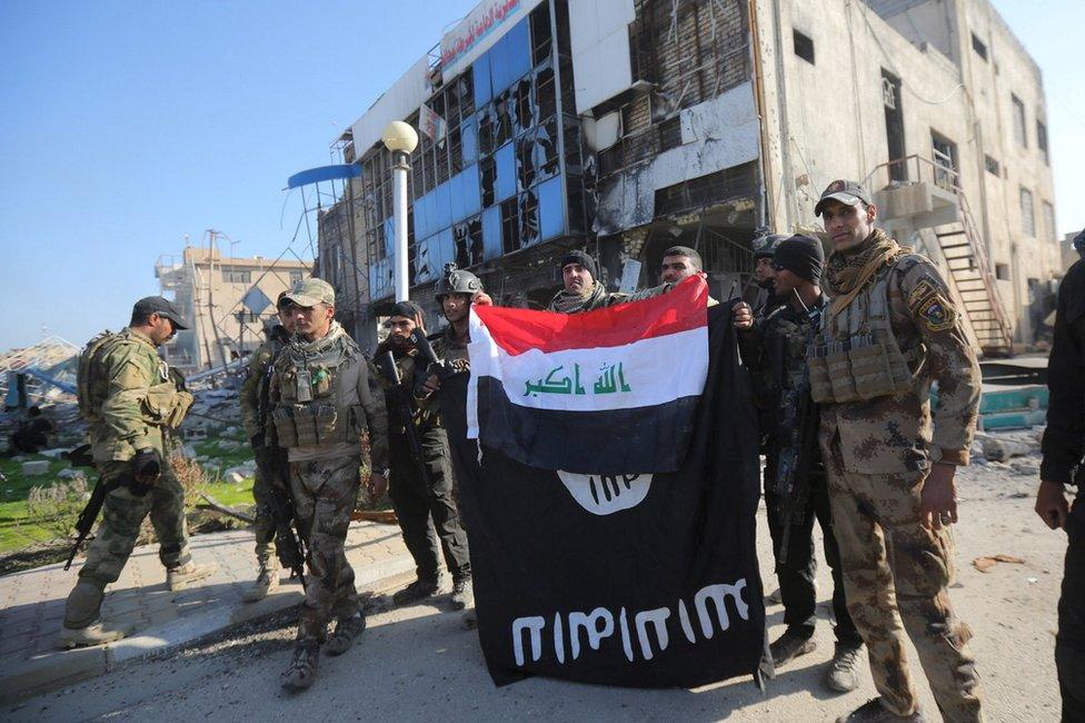 Iraqi security forces personnel hold up an Iraqi national flag over an upside-down Islamic State banner at the provincial government headquarters in Ramadi (28 December 2015)