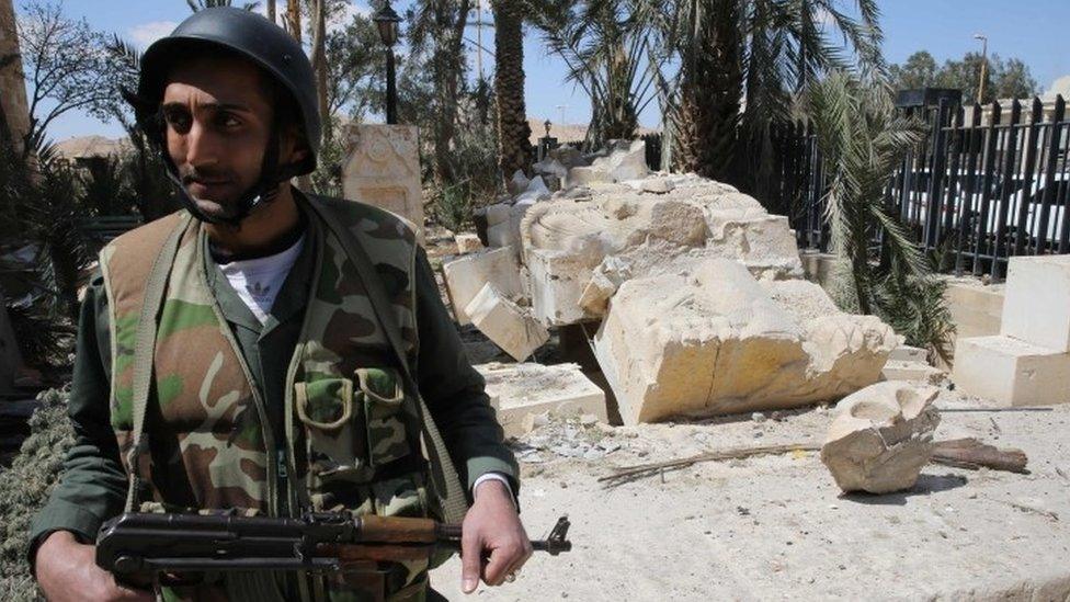 Syrian soldier guards the entrance to Palmyra"s museum next to the broken statue of the Lion of Palmyra in the ancient Syrian city