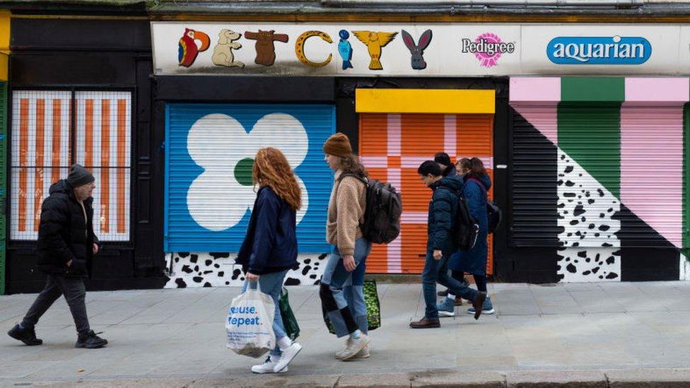 People walking passed closed shops with shutters down