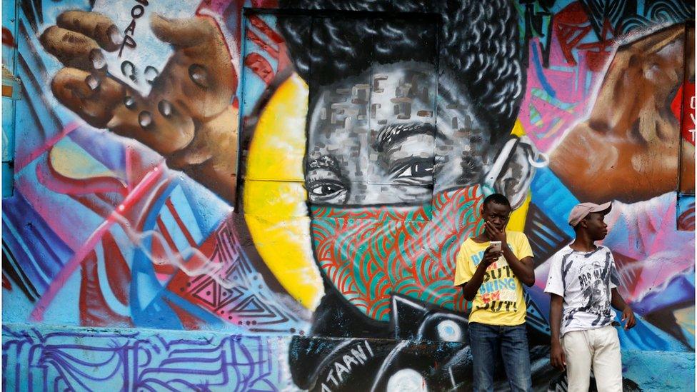 Residents stand in front of a graffiti by Mathare Roots"s youth group advocating against the spread of the coronavirus disease