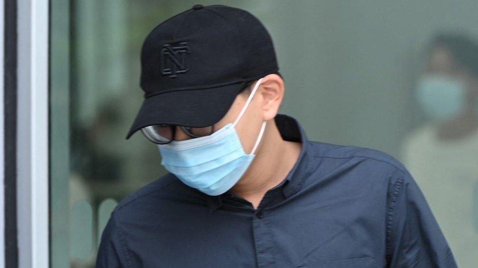 Derek Ng De Ren, pictured with his face covered by a baseball cap and a medical mask, outside court in 2021