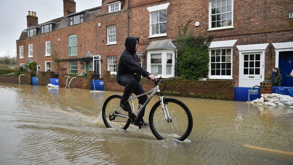 A man rides a bike through flood water, in Tewkesbury