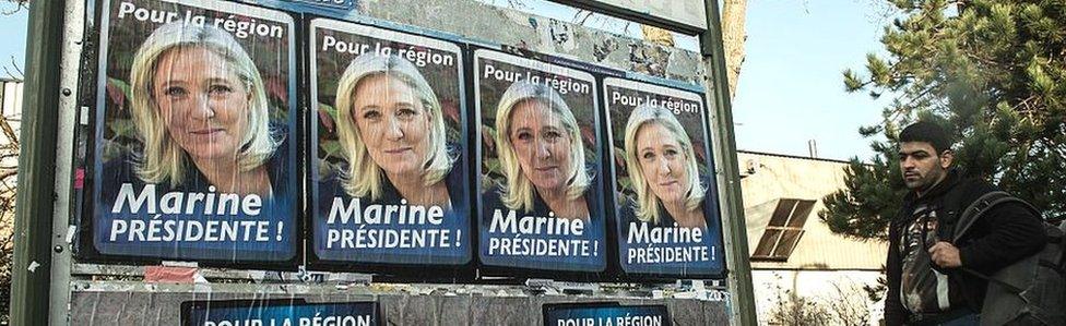 Migrant men walk past electoral posters of French far-right National Front (FN) party President Marine Le Pen in Calais on 7 December 2015