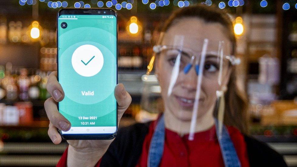 A bar worker holding a phone which is displaying a Covid-19 vaccine certificate