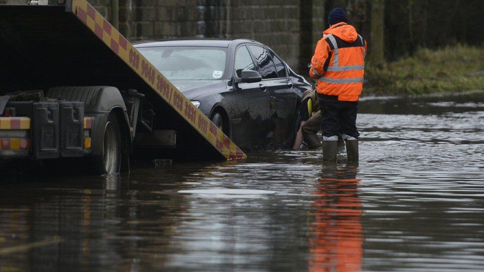 Vehicle recovery staff work to remove a car stranded on a flood-hit road