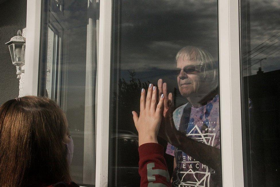 A young person holds their hand up to the window as a relative looks on from the other side