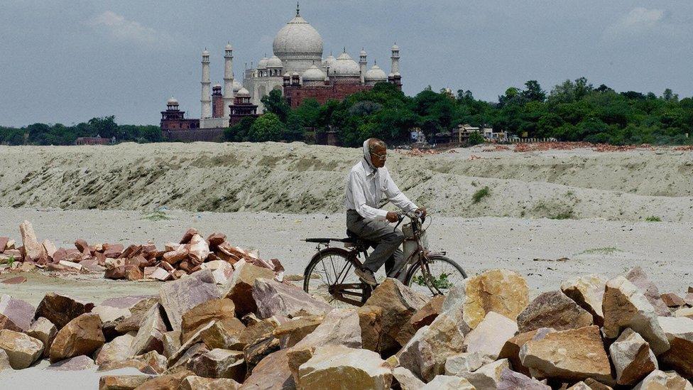 An Indian man rides a bicycle past rocks that were to be used at a construction near the Taj Mahal in 2003