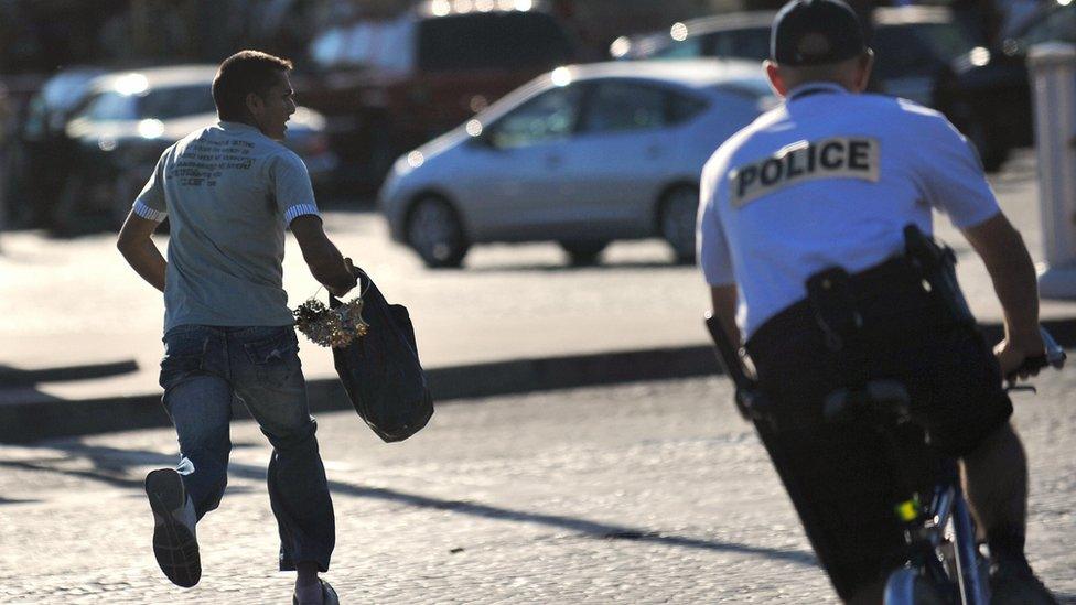 A street vendor who sells souvenirs runs away to evade a police patrol near the Eiffel tower in Paris