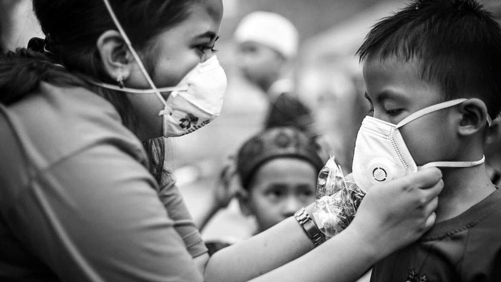 A volunteer helps a child put on an N95 face mask