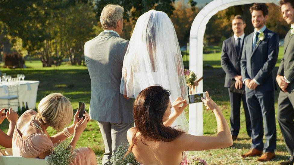 Guests taking photos on phones at a wedding